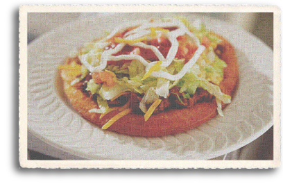A closeup up of a Navajo Taco: fry bread topped with fresh pinto beans, cheese, lettuce, onions, tomatoes and salsa. This is a very popular Northern New Mexico dish that gets served up at the annual world famous Indian Market in Santa Fe, New Mexico.